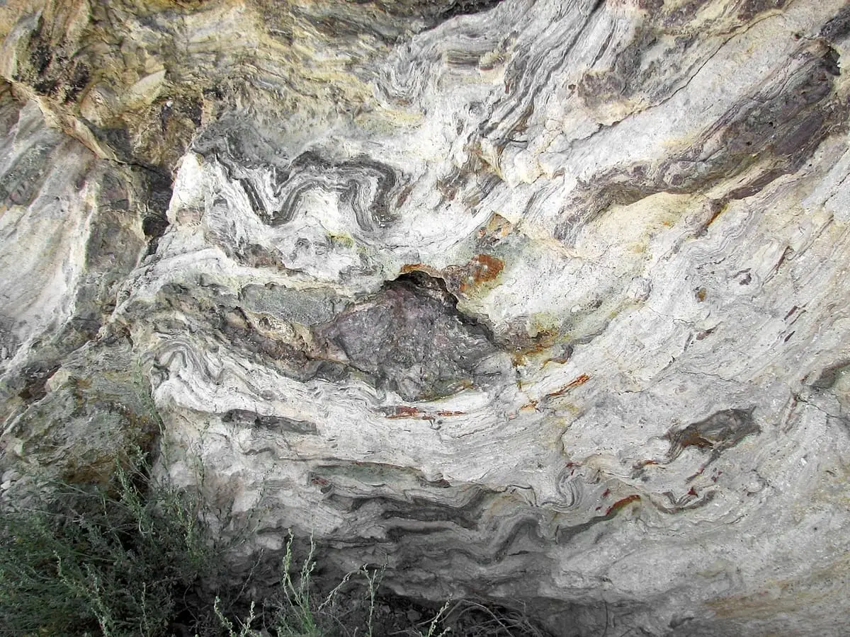 Swirling flow banded rhyolite rock face in Hot Creek Gorge with pale and rusty layers