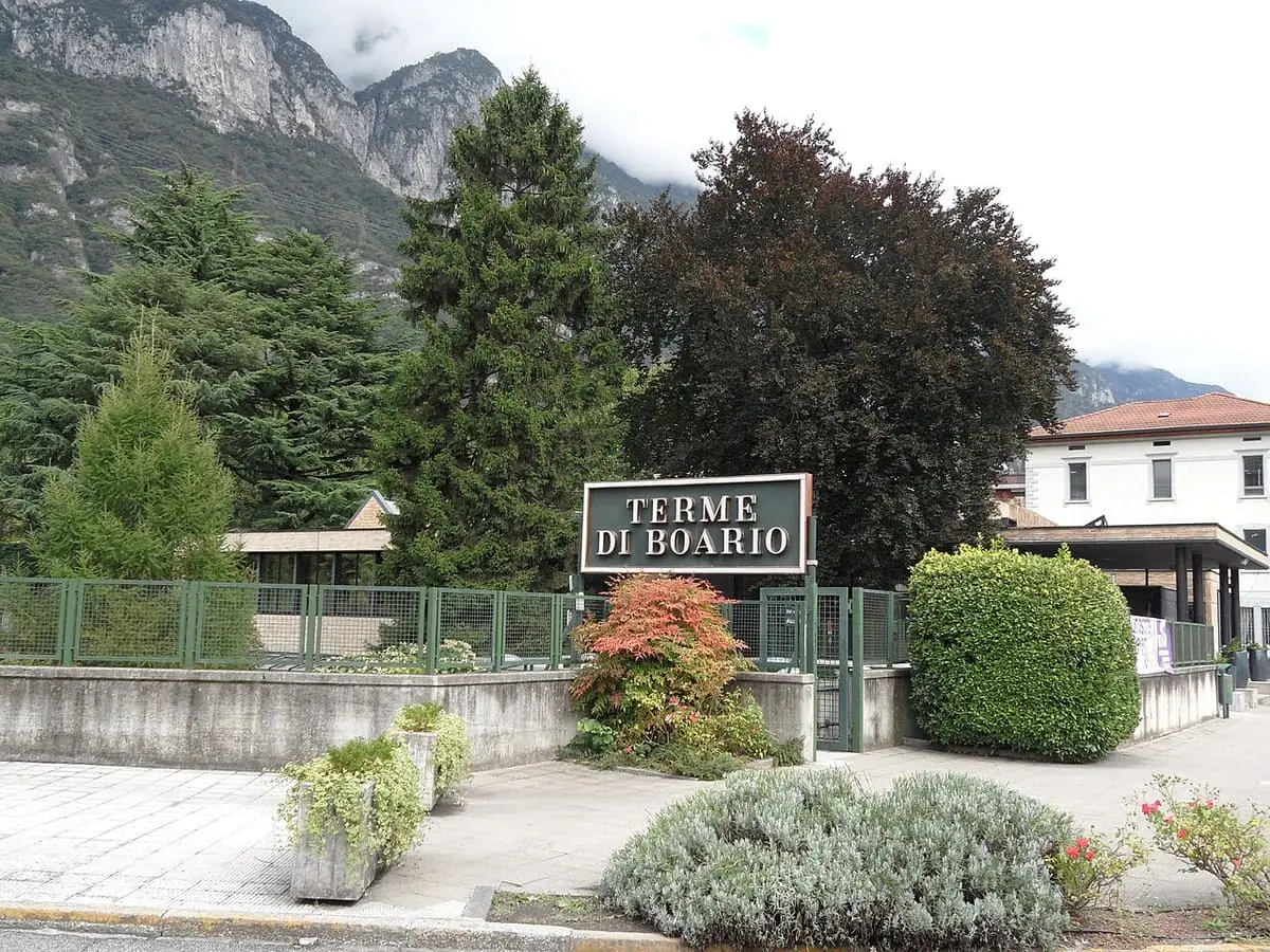 Terme di Boario entrance sign among shrubs and trees with mountains behind