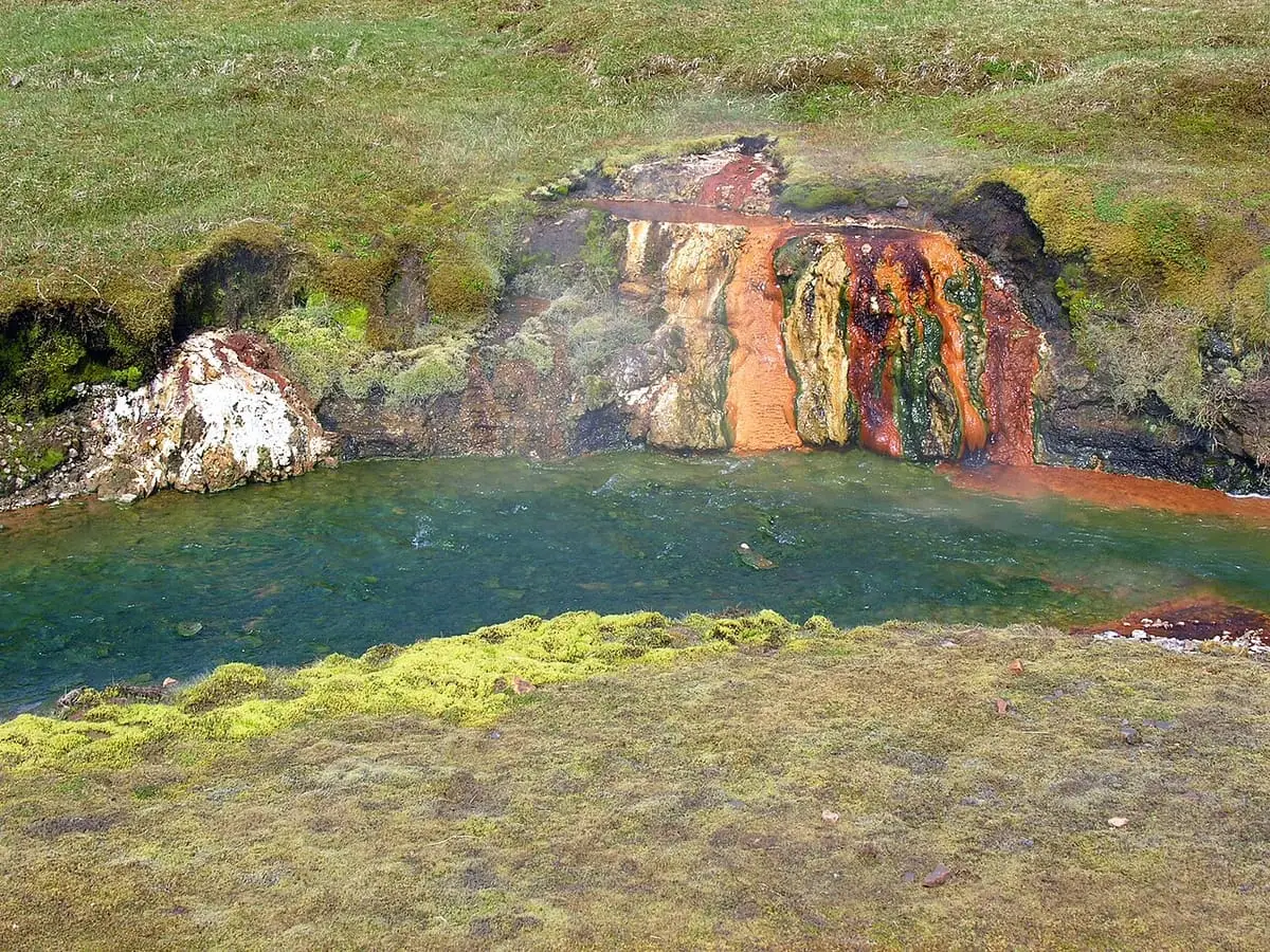 Hot spring pool with orange and white mineral deposits in the Reykjadalur valley
