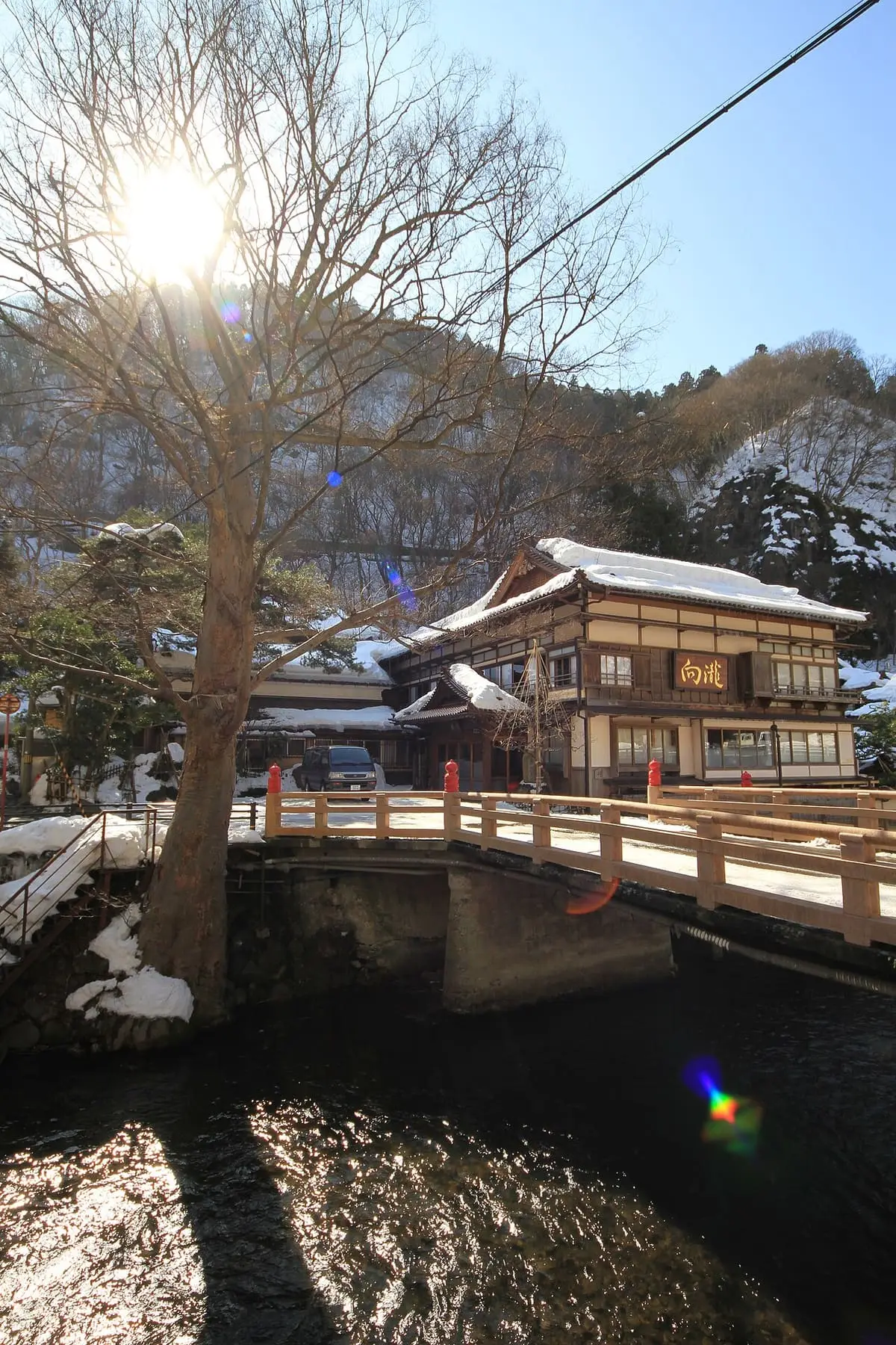 Wooden inn and bridge over the river at Higashiyama Onsen beneath a bare winter tree
