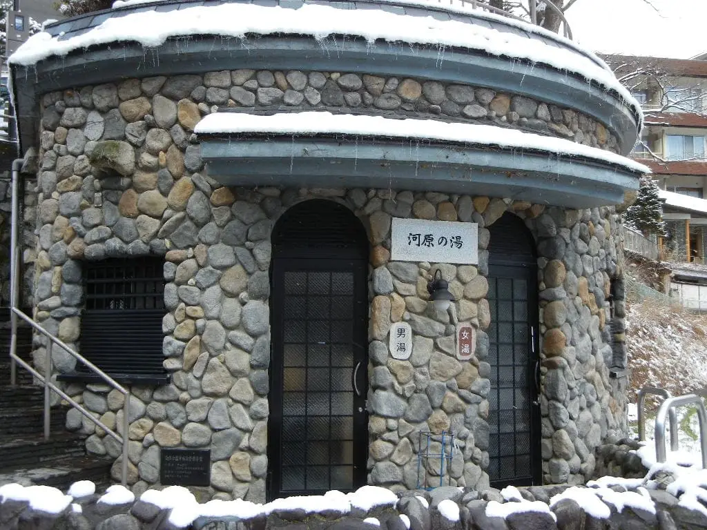 Round stone Kawara no Yu public bathhouse at Shima Onsen with snow on the ground