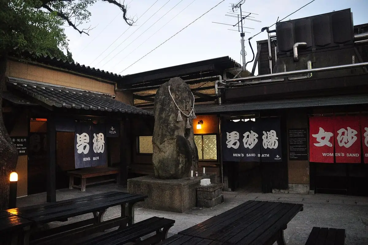Wooden facade and stone monument at the entrance of Hyotan Onsen bathhouse in Beppu at dusk
