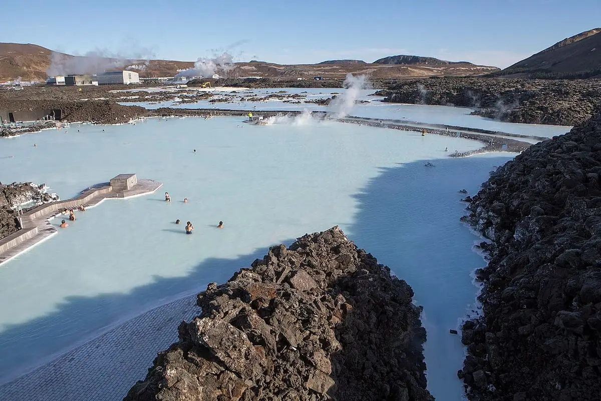 Wide milky blue Blue Lagoon between lava rock walls with steam rising in the distance