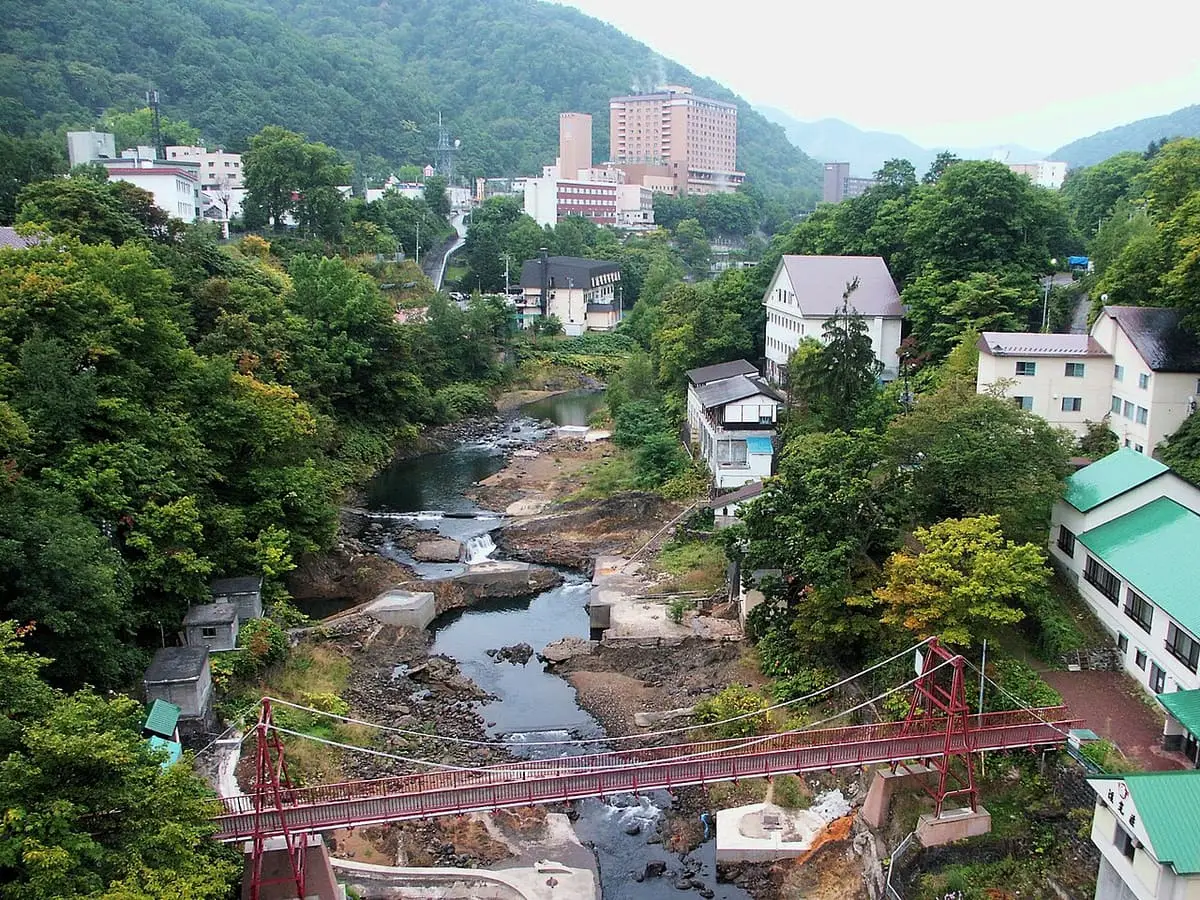 Toyohira River winding through the green Jozankei valley past a red suspension bridge and hotels