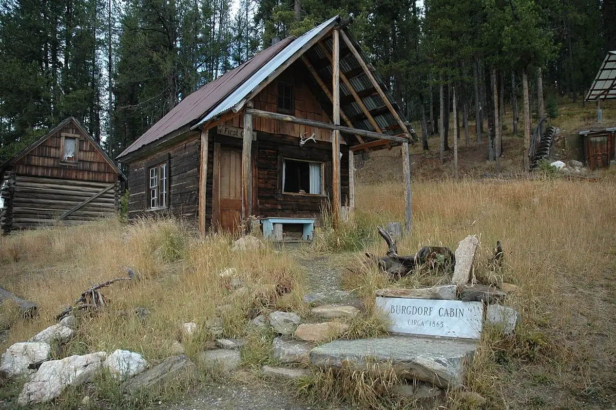Old Burgdorf log cabin with a stone path and engraved sign under tall pines