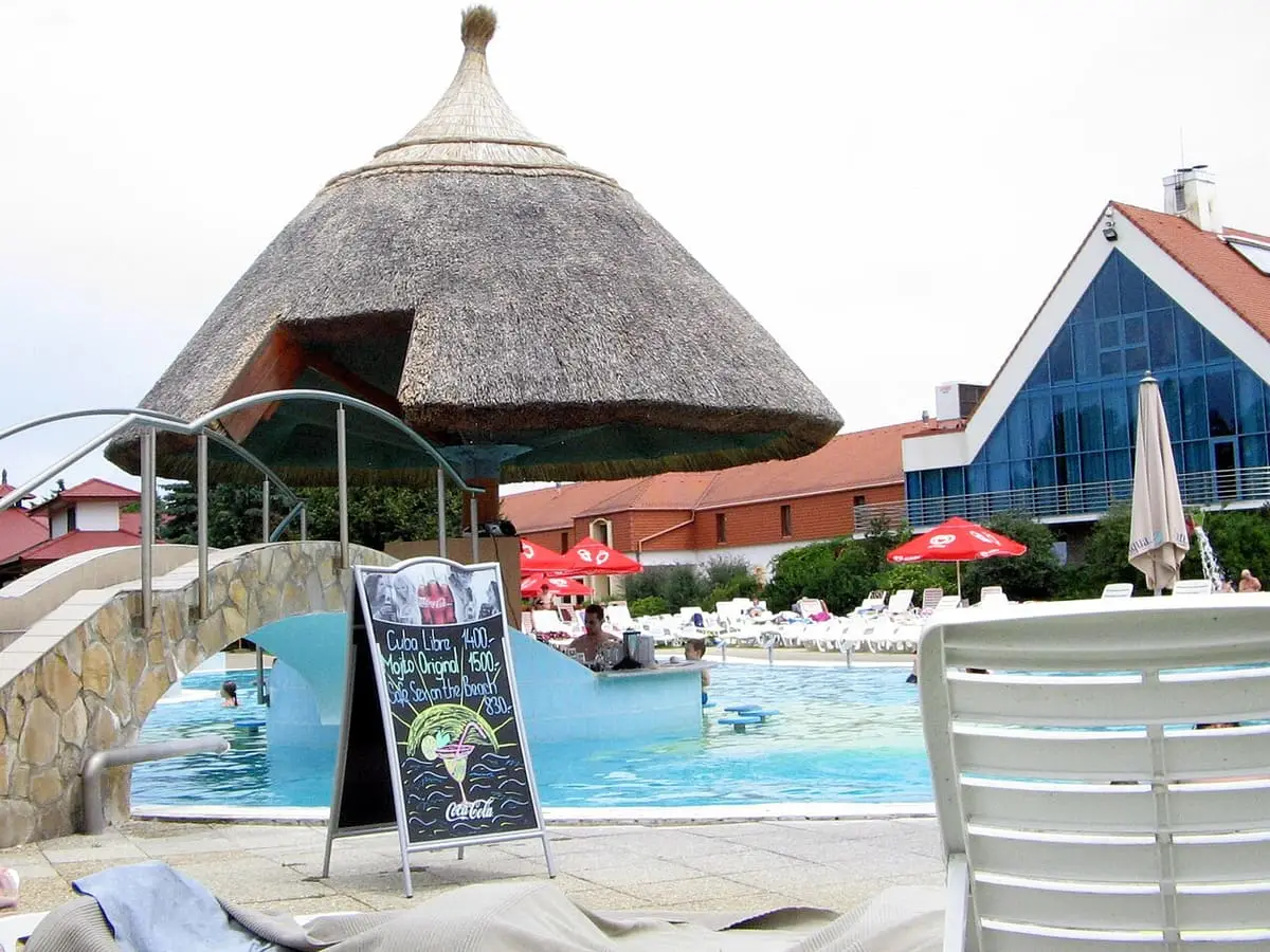 Thatched cone roofed bar beside a pool and footbridge at Kehida Termál