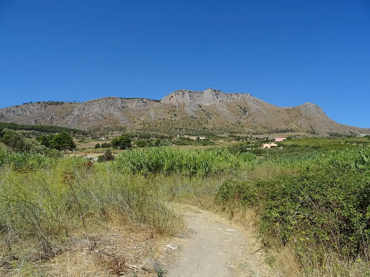 Dirt path through dry scrub and fields with a limestone ridge above the Terme Segestane area