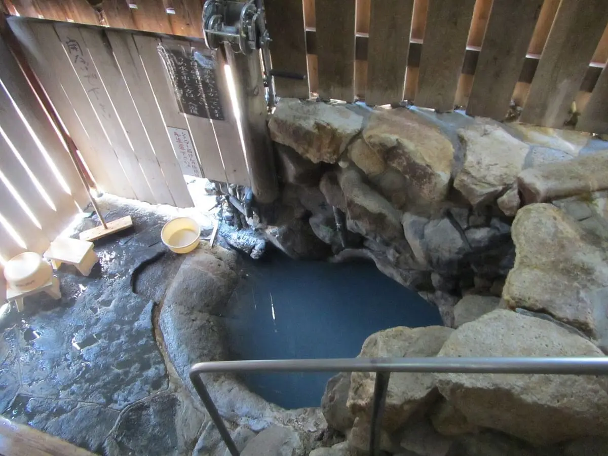 Milky blue hot spring pool inside the wooden and rock walls of the Tsuboyu hut