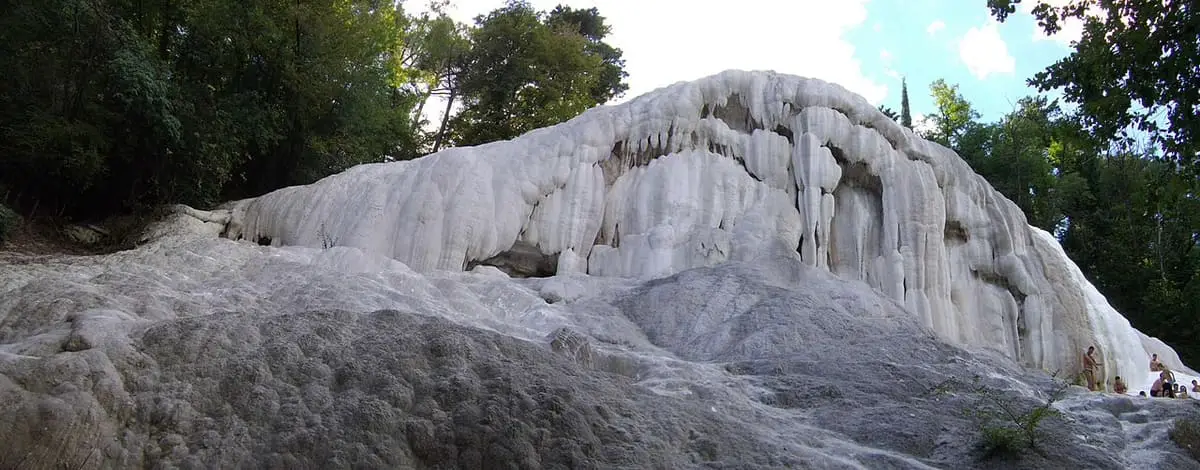 Rounded white travertine mound of the Balena Bianca against woodland at Bagni San Filippo
