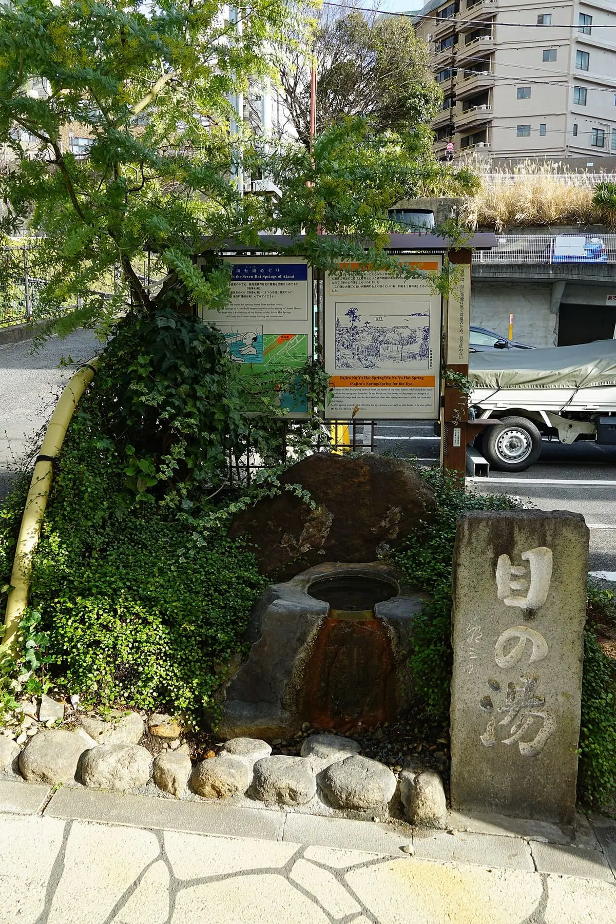 Stone monument and small spring basin at Sajiro no Yu among greenery in Atami Onsen