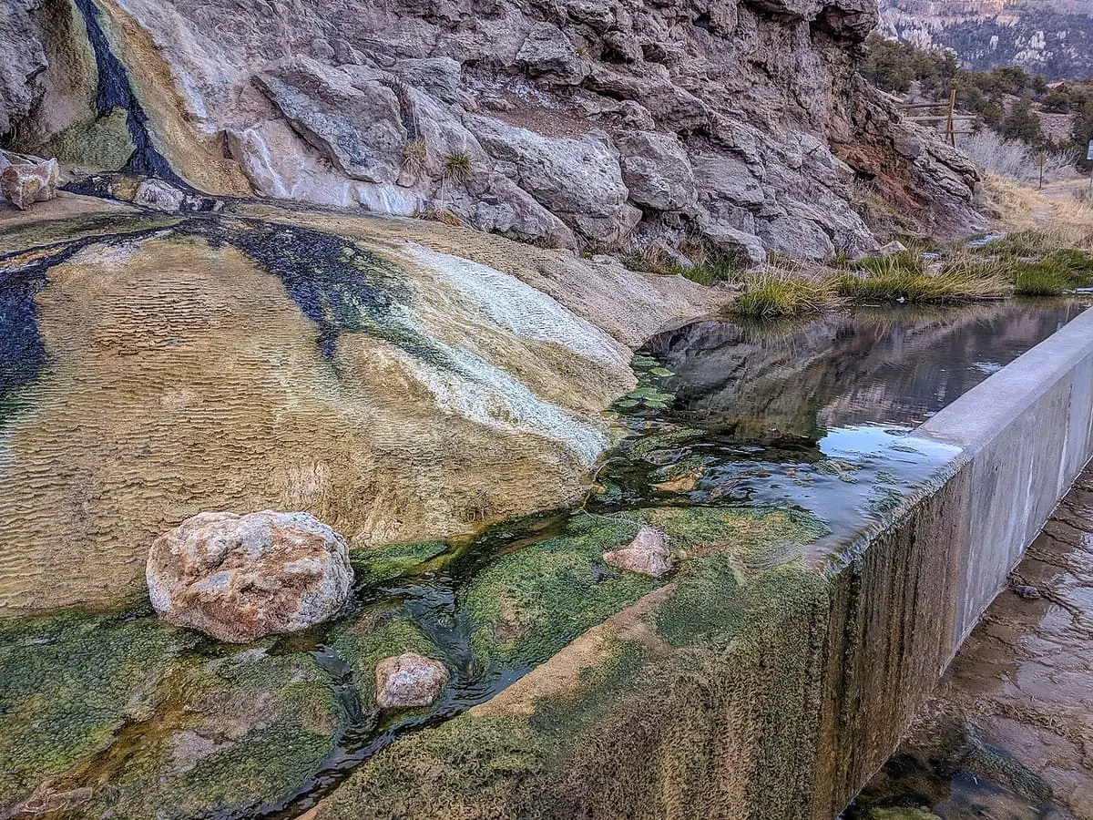 Mineral spring water trickling over colorful travertine deposits beside a concrete channel at Soda Dam
