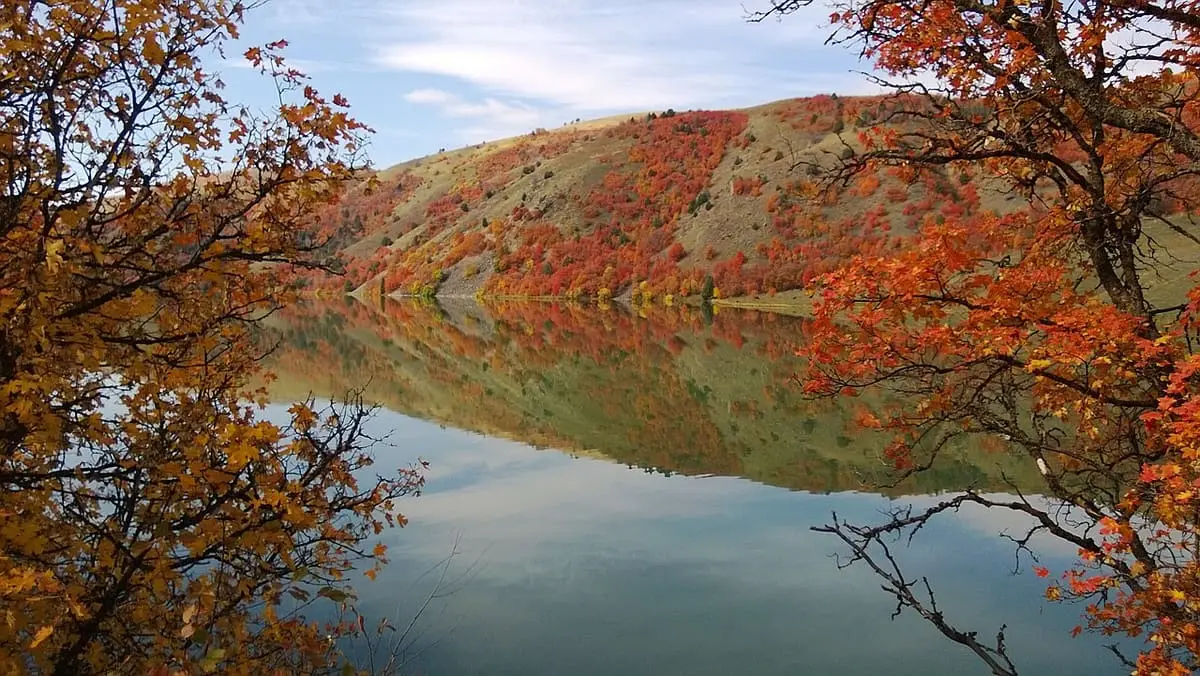 Autumn trees framing a still reservoir and reflected hills in Franklin County, Idaho