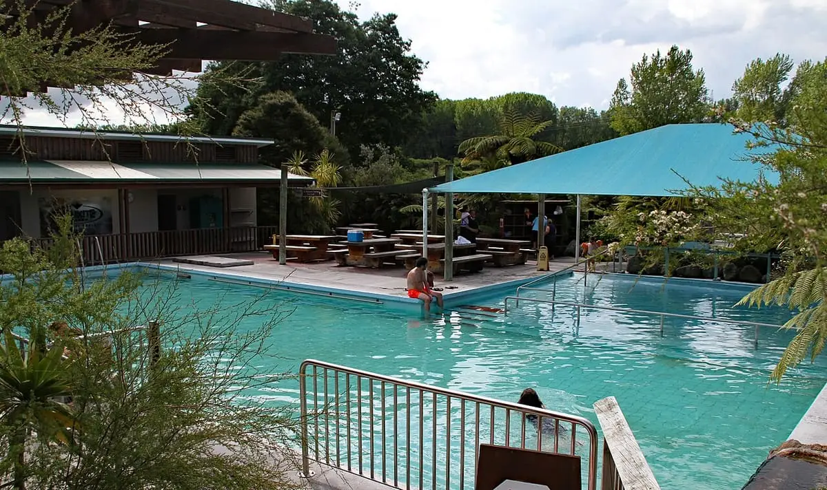 Large turquoise outdoor thermal pool at Waikite Valley with picnic tables and a shade canopy