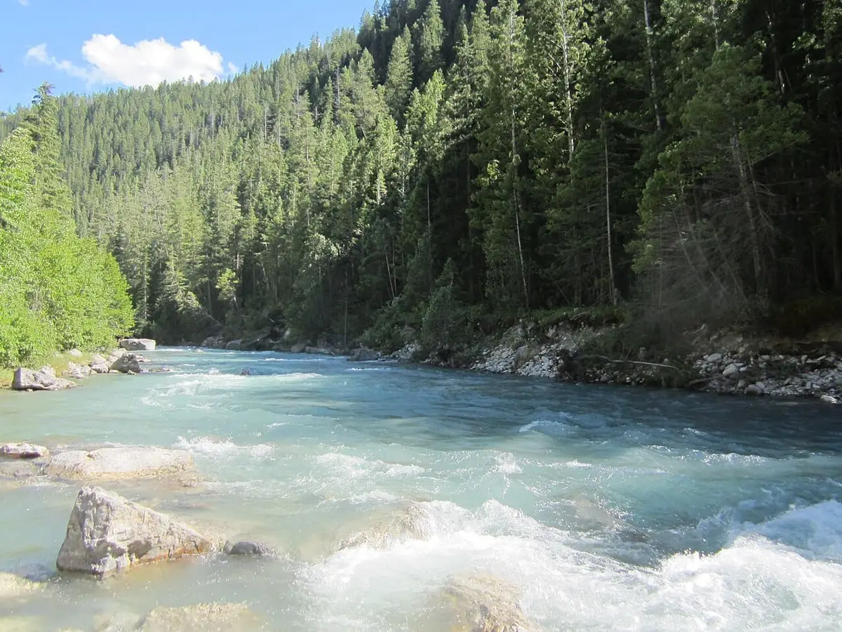 Turquoise Lussier River rushing past boulders below forested slopes near Lussier Hot Springs