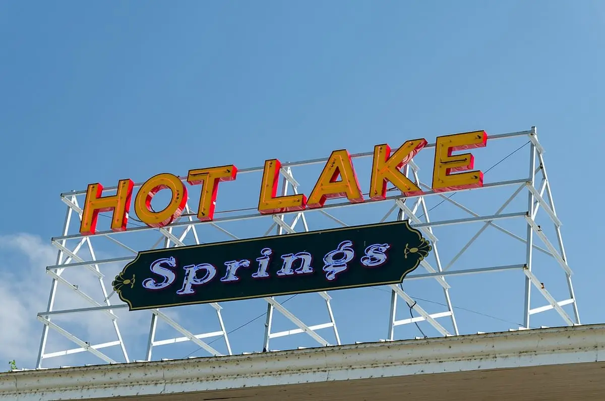 Orange Hot Lake Springs neon sign on a white metal frame against a blue sky