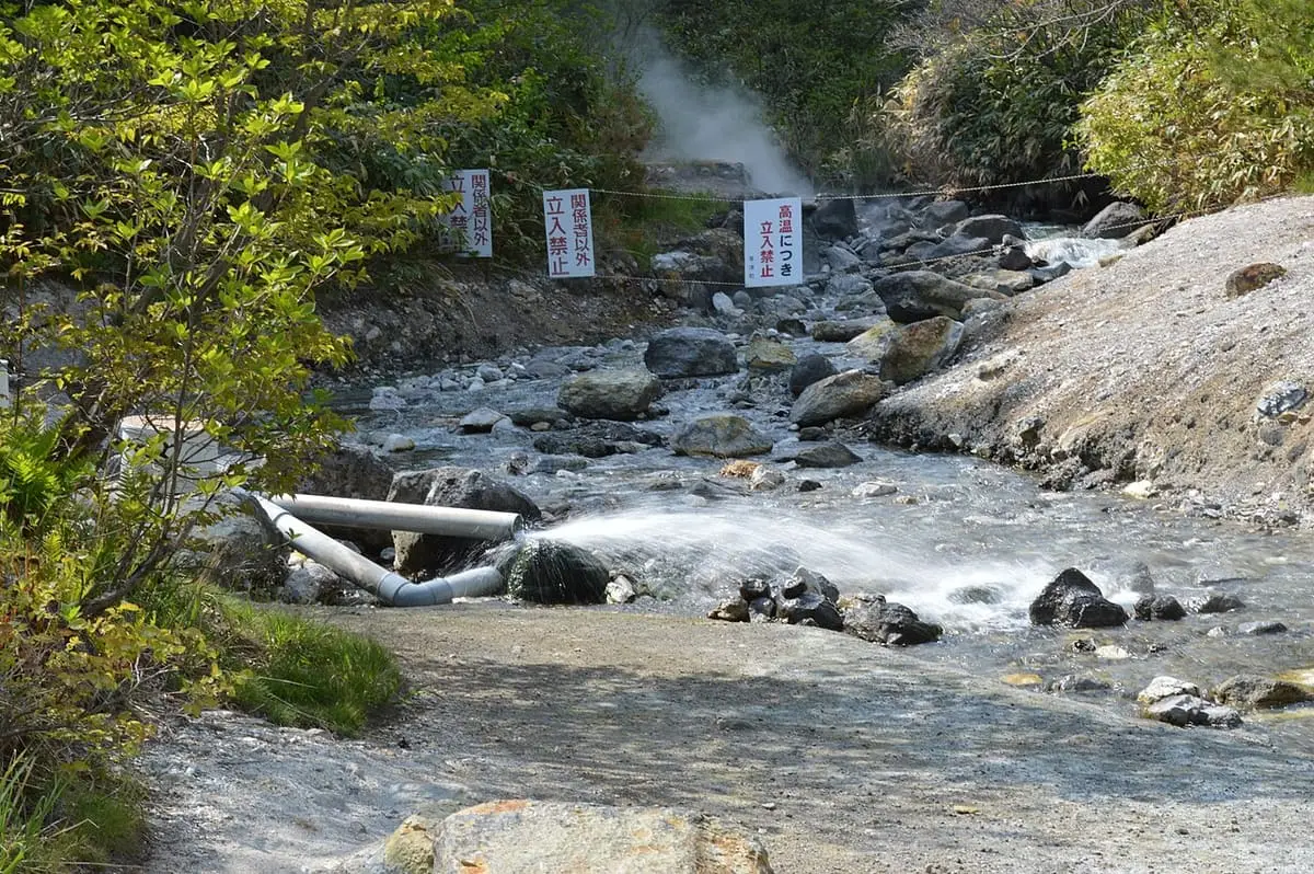 Hot stream flowing over rocks with steam in Sainokawara Park