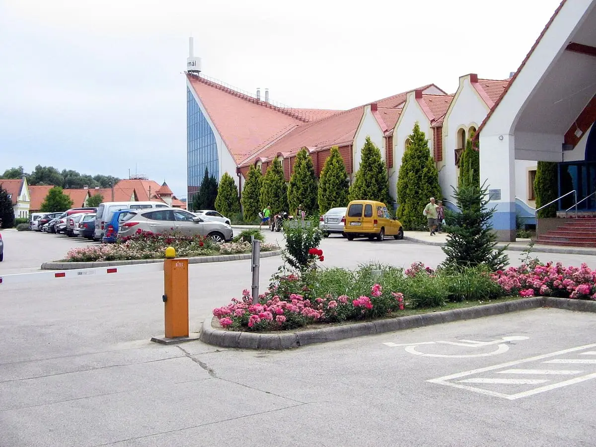 Red roofed Kehida Termál building with flower beds beside its car park