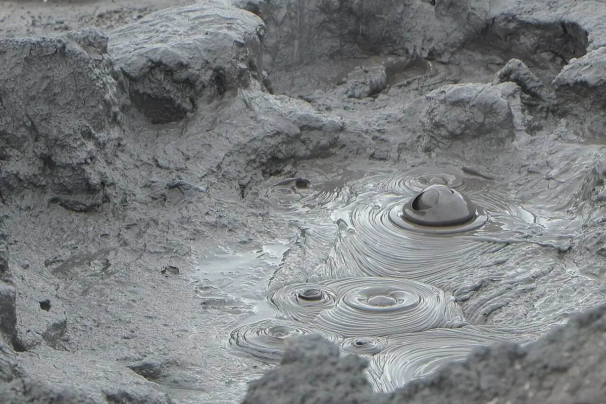 Grey bubbling mud pool with a bursting bubble and ripples in the Hell's Gate thermal area