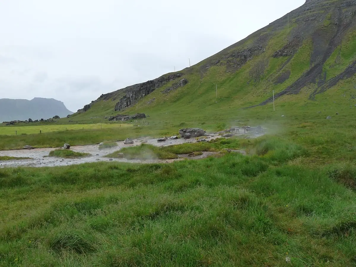 Steam rising from the hot springs in a green valley that fill Krossneslaug