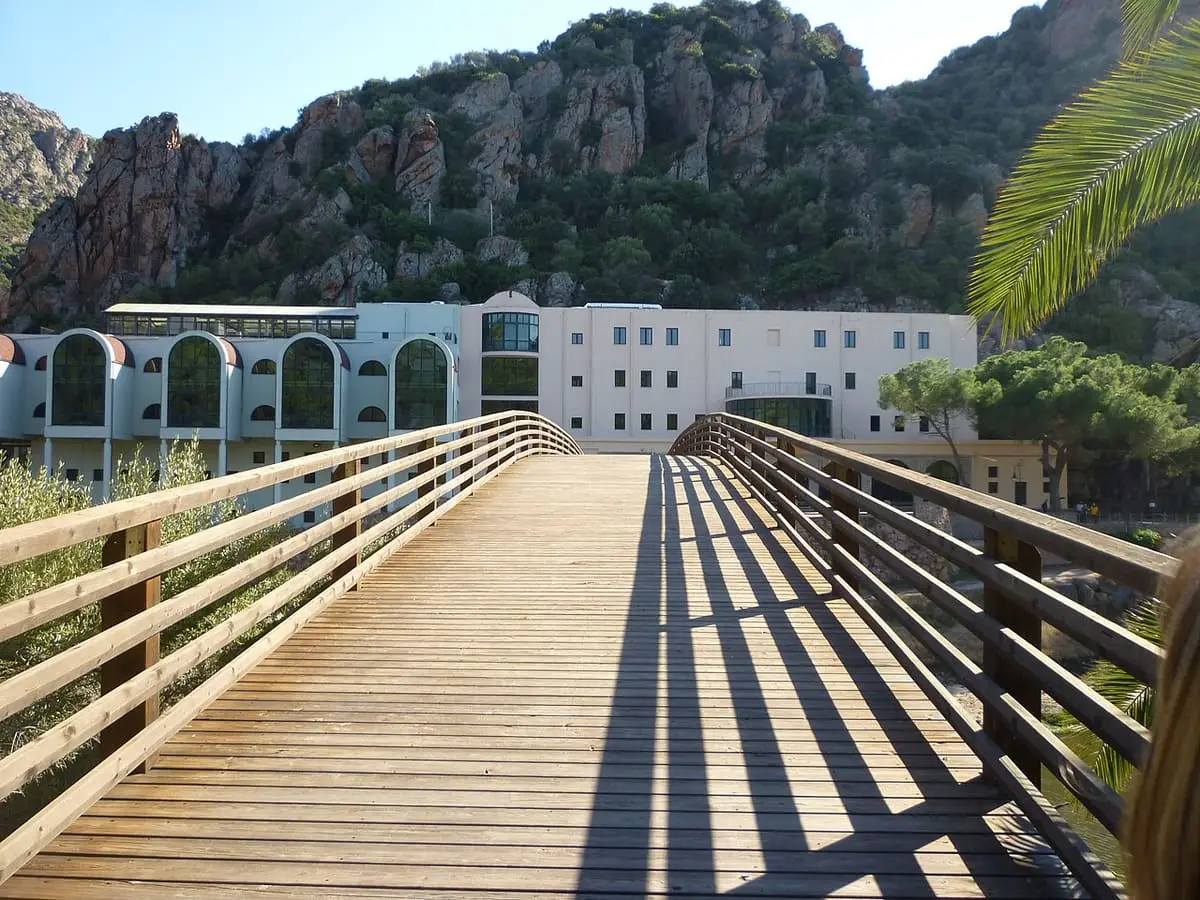 Wooden footbridge leading to the Casteldoria spa building below rocky hills