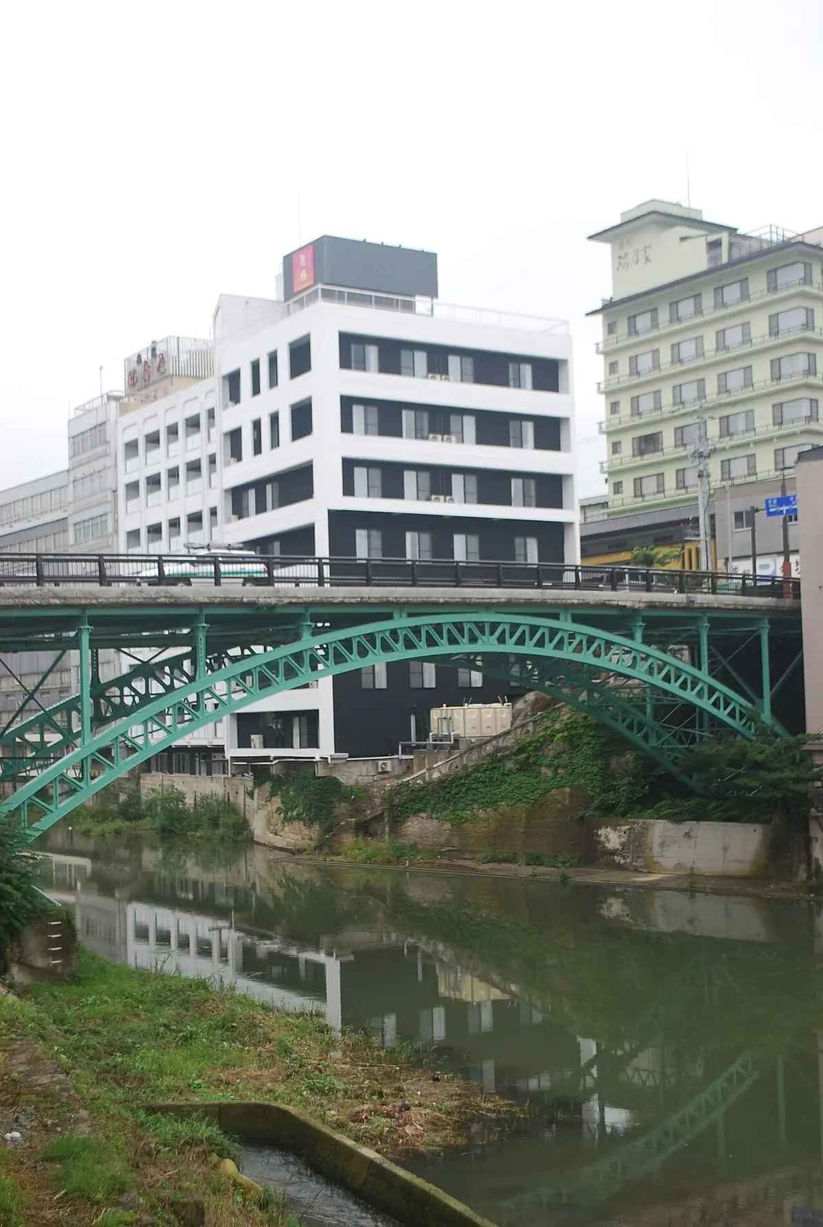 Green arched Totsuna Bridge over the river at Iizaka Onsen with hotels behind