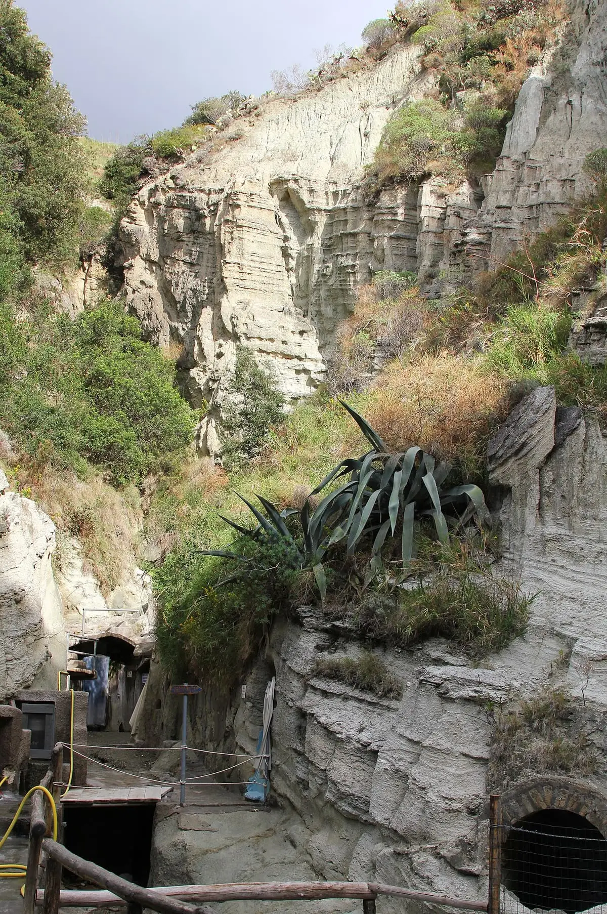 Entrance to Terme di Cavascura at the foot of a tall gorge with agave plants
