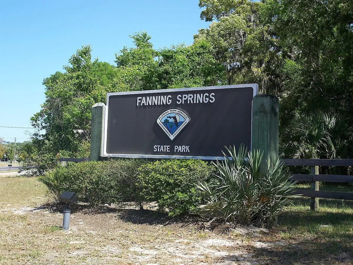 Fanning Springs State Park entrance sign beside shrubs and a wooden fence