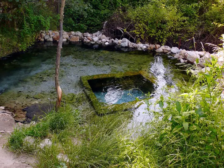 Clear hot spring pool edged with stones and green plants at Loutra Eleftheron near Kavala