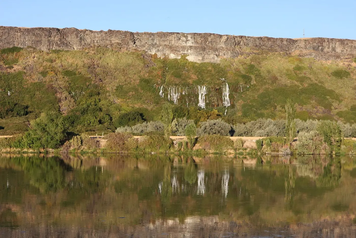 Spring water spilling from the Thousand Springs basalt cliffs and reflected in the Snake River near 1000 Springs Resort
