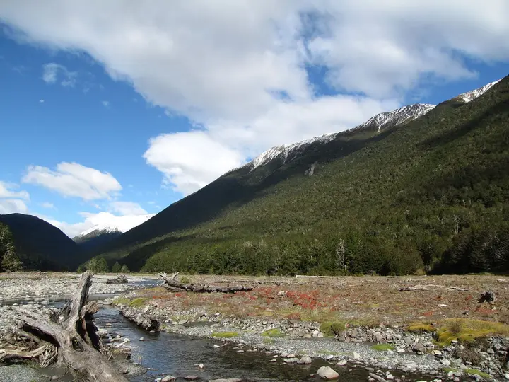 Maruia River flowing over a stony bed below forested slopes and snowy peaks near Maruia Springs