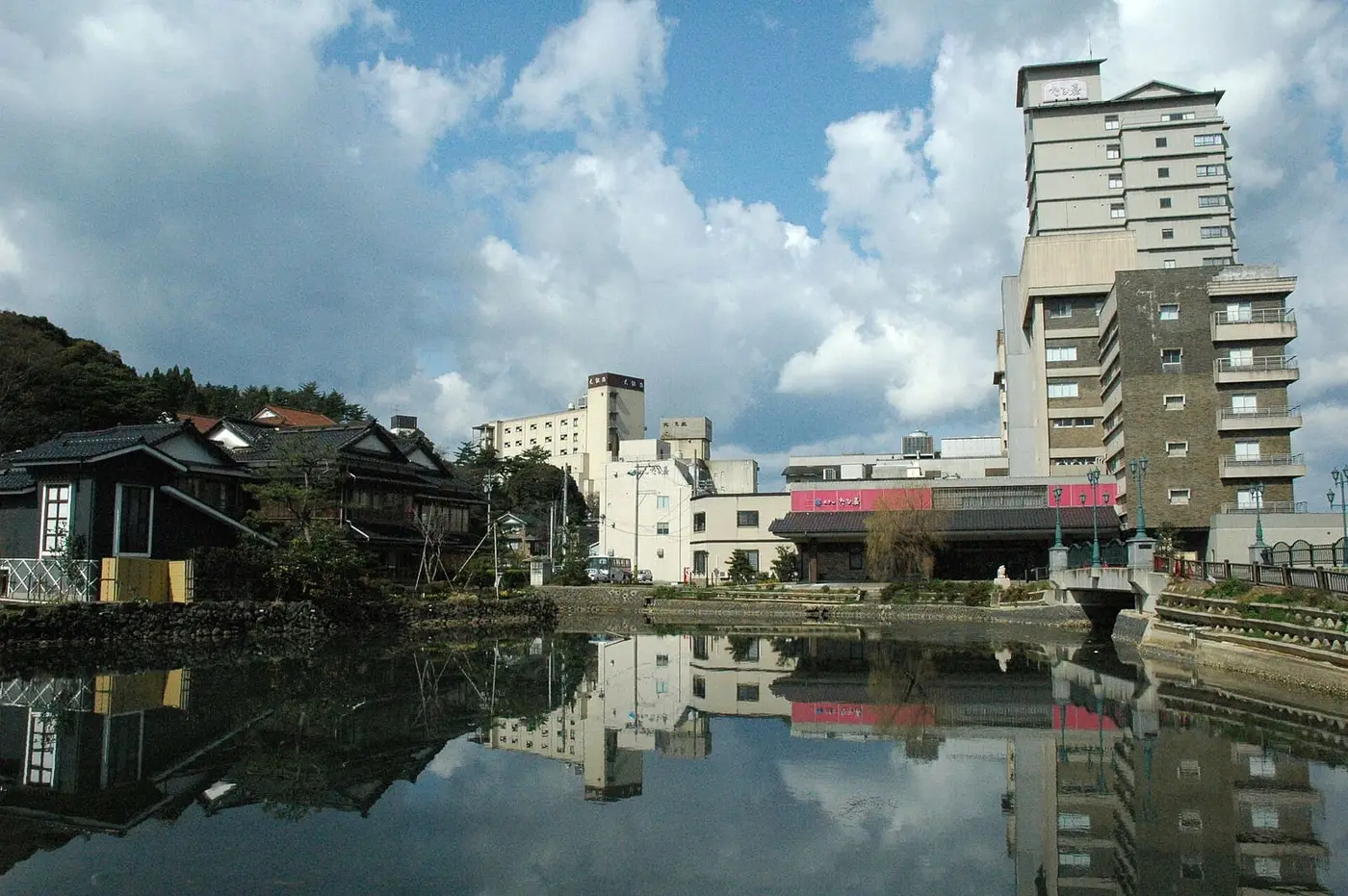 Hotels of Wakura Onsen reflected in still water under a cloudy blue sky