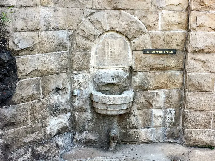 Arched stone fountain niche with a spout and a Dripping Spring nameplate in an old stone wall