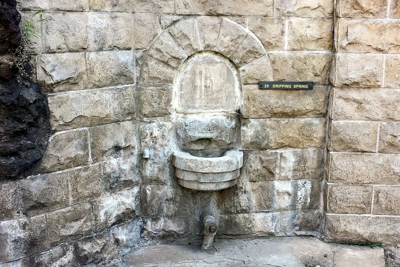 Arched stone fountain niche with a spout and a Dripping Spring nameplate in an old stone wall