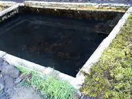 Square concrete soaking tub at Lower Breitenbush Hot Springs edged with moss, grass and rocks