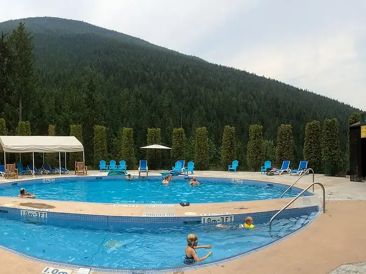 Outdoor hot pool at Nakusp Hot Springs surrounded by green buildings and a forested hill