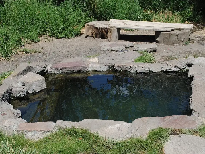 Stone lined soaking pool known as The Cube at Montezuma Hot Springs with a wooden bench behind