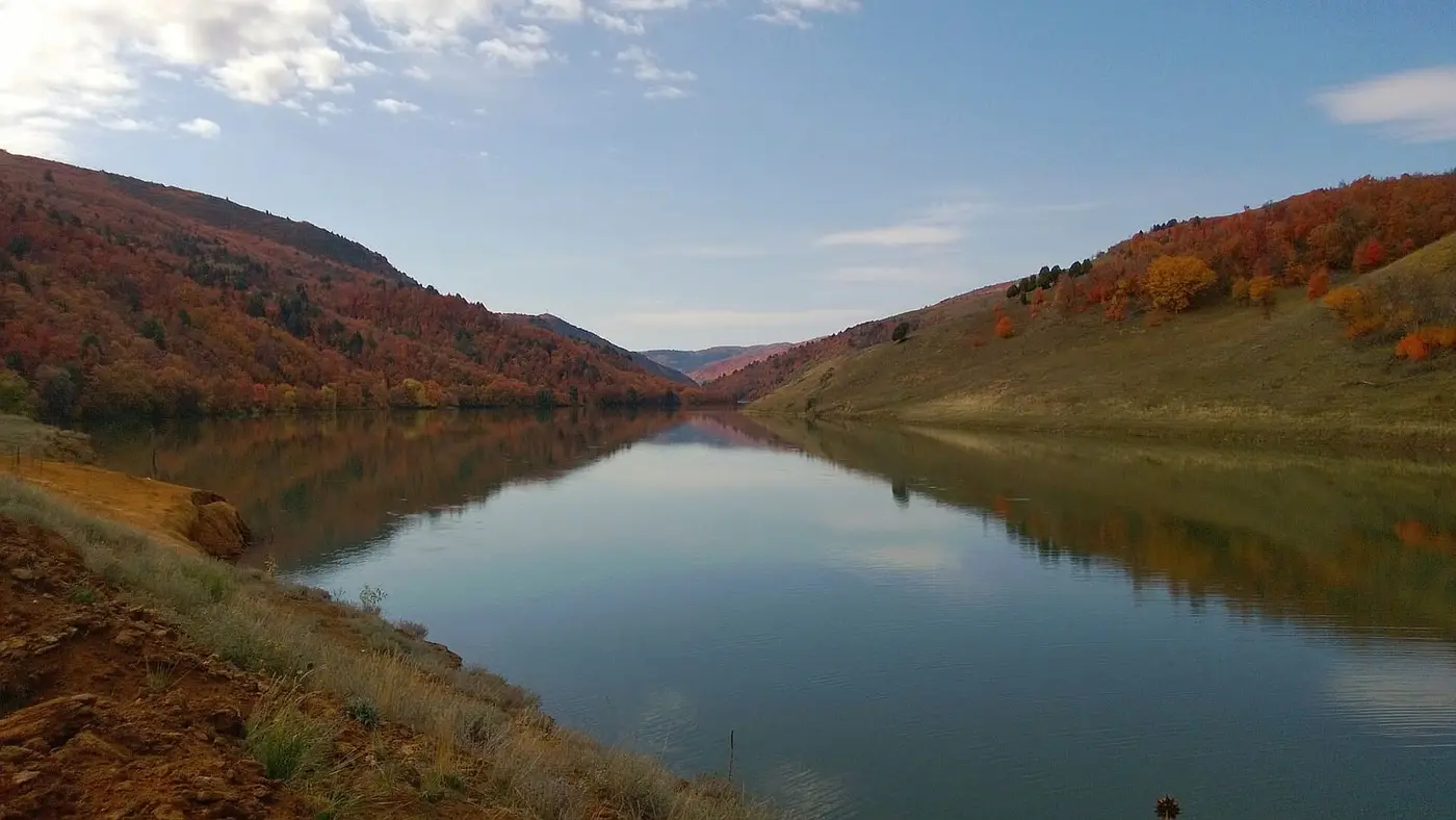 Calm reservoir water reflecting autumn hillsides in the valley near Maple Grove Hot Springs