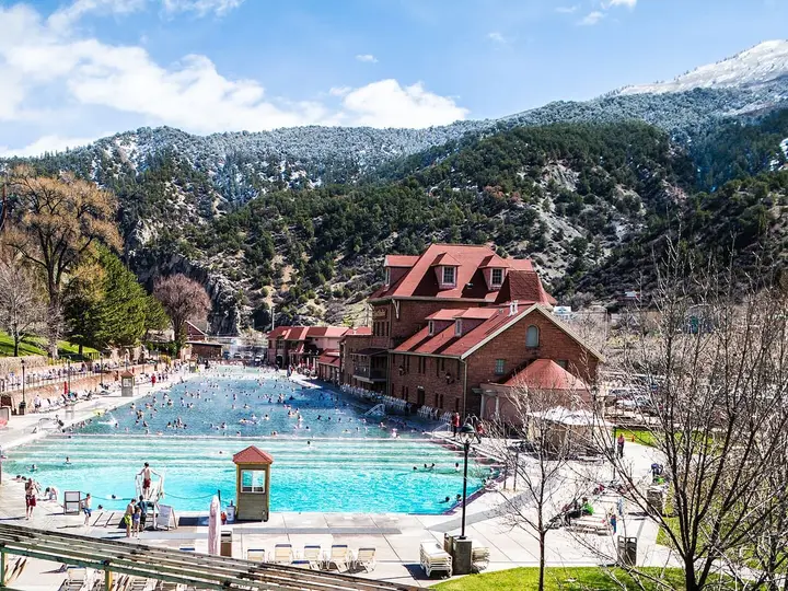 Glenwood Hot Springs Pool with its red roofed bathhouse below snow dusted mountains on a sunny day