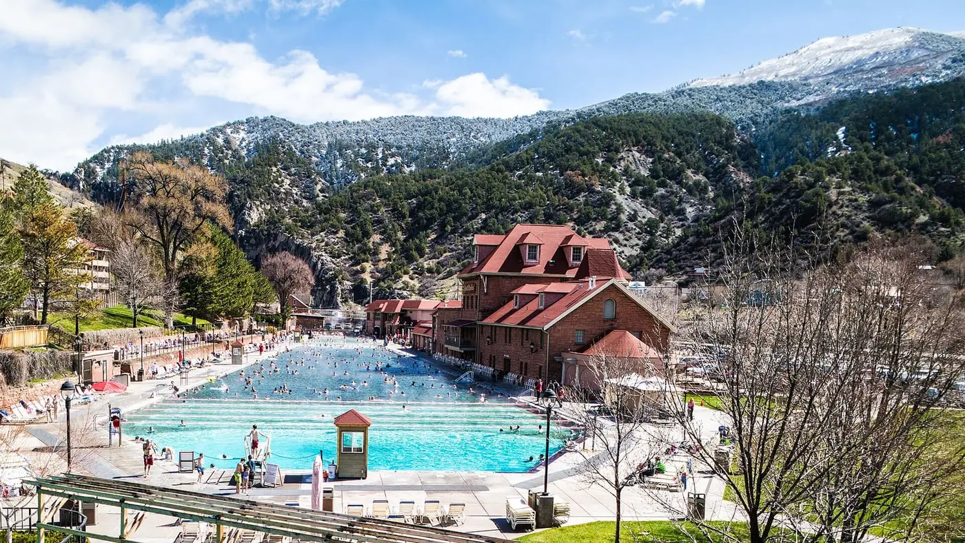 Glenwood Hot Springs Pool with its red roofed bathhouse below snow dusted mountains on a sunny day