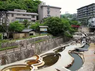 Stone channels and pools along the river walk through Arima Onsen beneath hotels and green hills