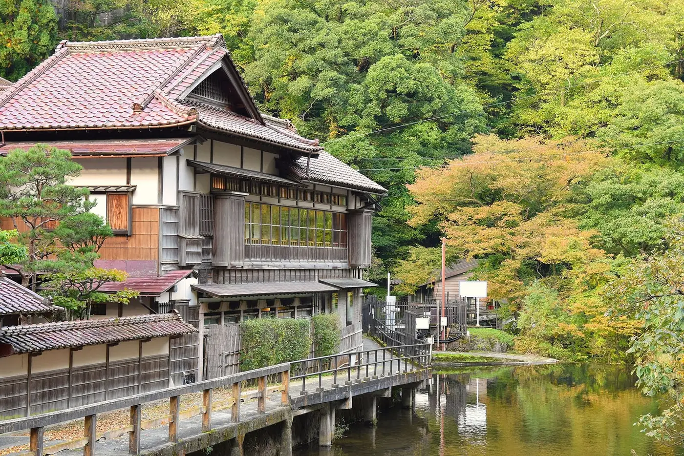 Traditional wooden inn beside a calm river and green hillside at Higashiyama Onsen