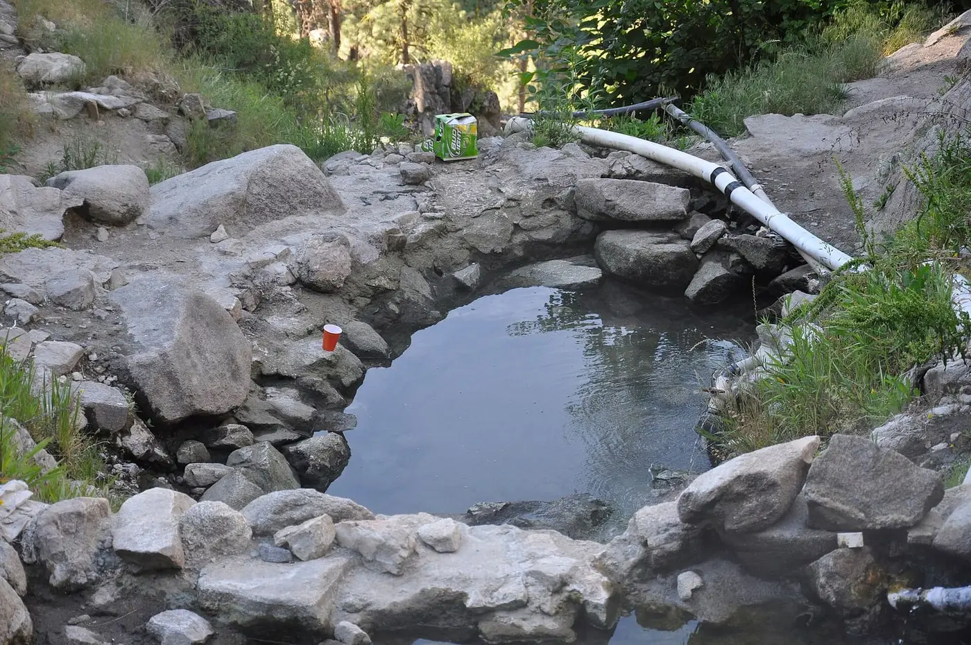 Rock rimmed soaking pool fed by white piping at Skinny Dipper Hot Springs