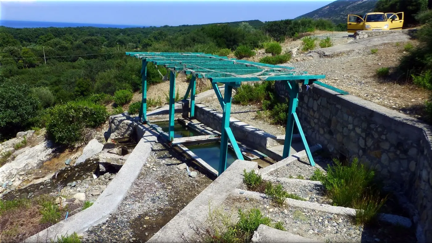 Small open air thermal pool under a green pergola among hillside shrubs at Therma, Samothraki