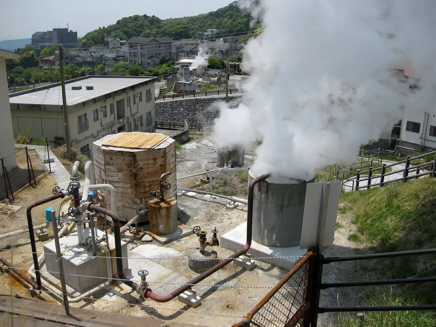 Steam billowing from hot spring wellheads and pipes among buildings at Kirishima Onsen