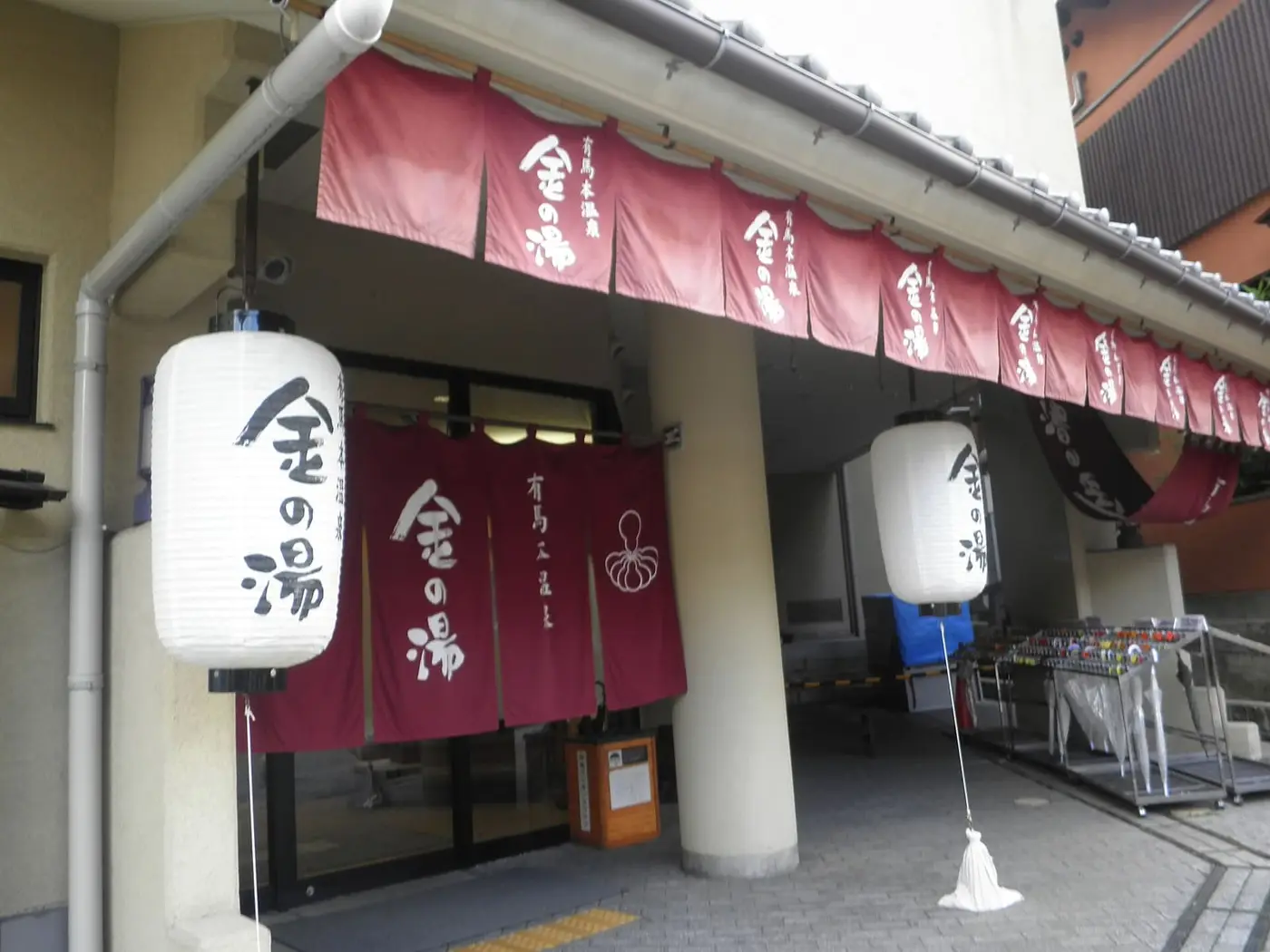 Entrance of Kin no Yu bathhouse in Arima Onsen with red noren curtains and white paper lanterns
