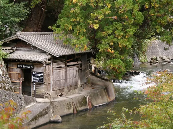 Wooden riverside bathhouse beside the rushing Tanohara River at Kurokawa Onsen in autumn