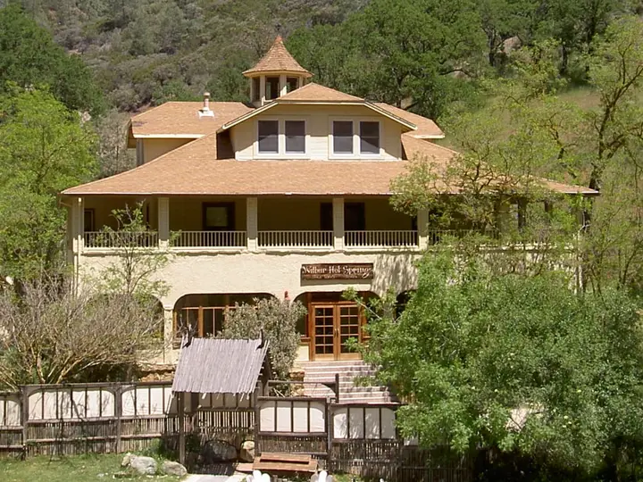 Front of the historic Wilbur Hot Springs lodge with wraparound porch below wooded hills