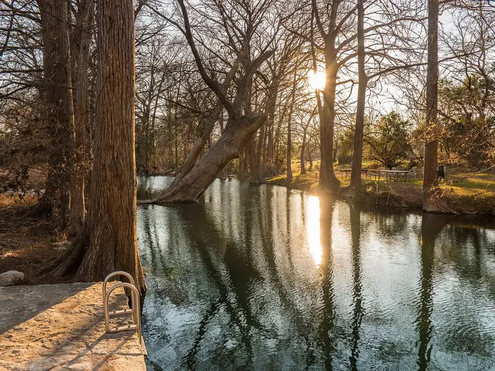 Cypress Creek swimming hole at Blue Hole Regional Park with tall cypress trees and low sun