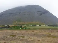 Grey mountain rising above the farmland at Hoffell in southeast Iceland under low cloud