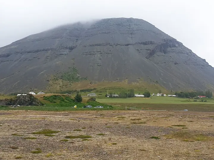 Grey mountain rising above the farmland at Hoffell in southeast Iceland under low cloud